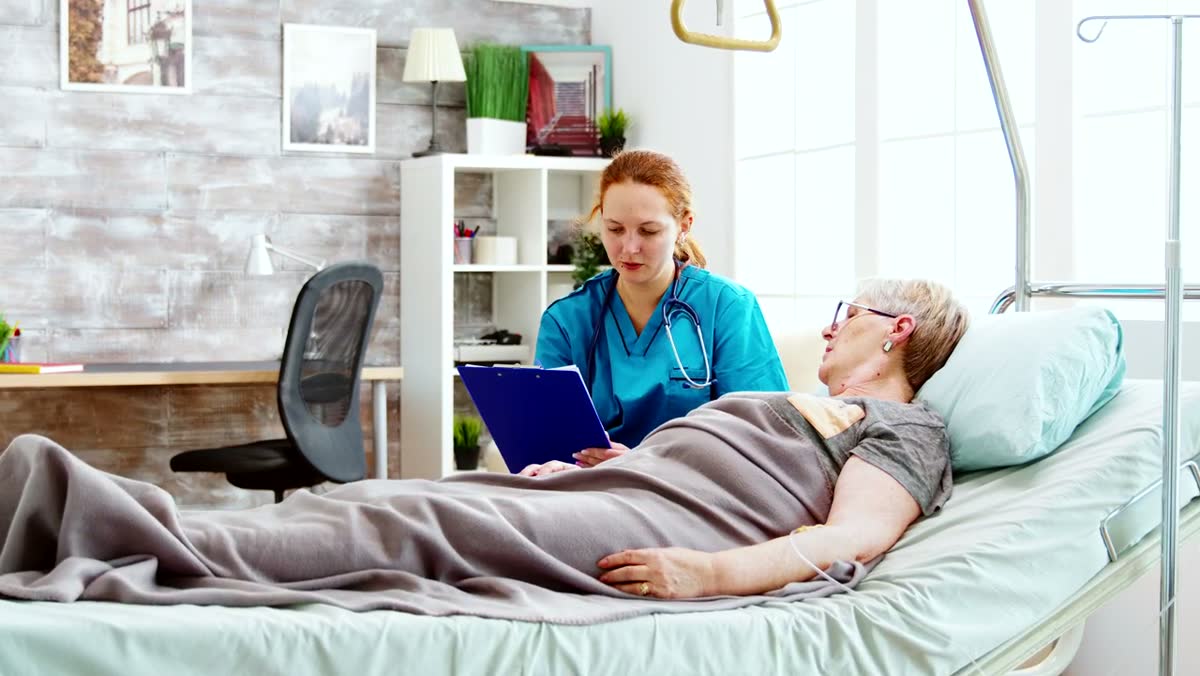 A nurse charting on a tablet at a patient's bedside